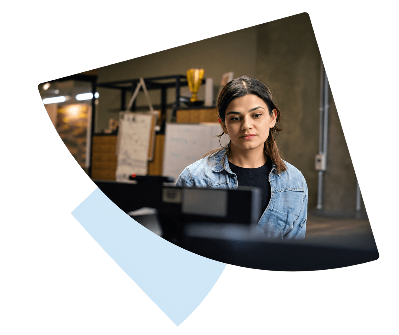 Young woman in denim jacket intently working on a computer in an office.