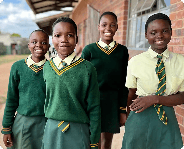 Four smiling female students in green and yellow school uniforms stand outdoors.