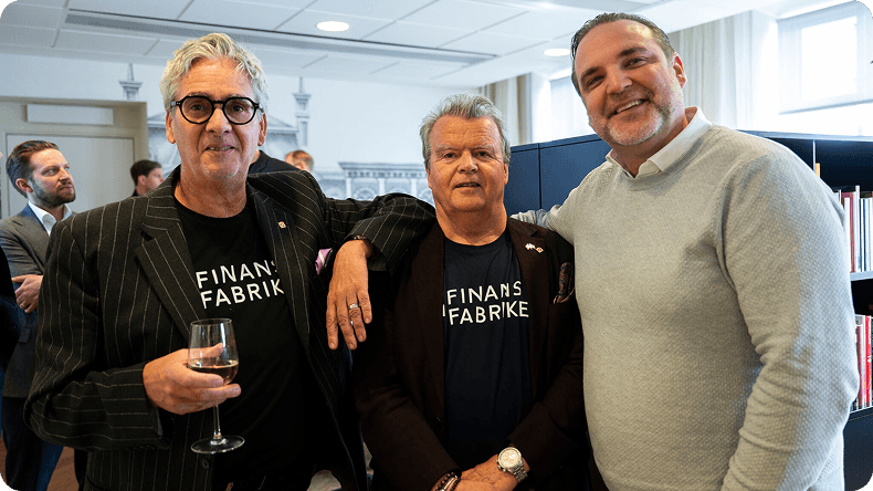 Three smiling men at an event, two wearing "FINAN FABRIK" t-shirts.