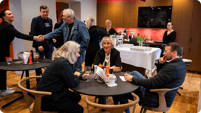 People socializing at a business event, some shaking hands, others sitting at tables.
