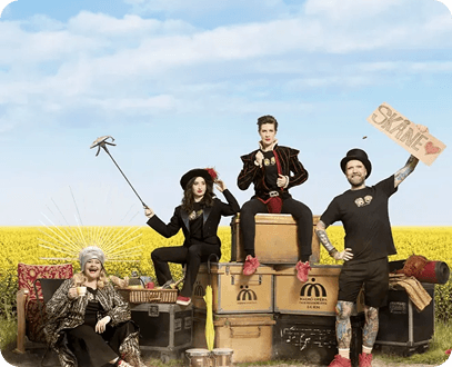 Four diverse people pose on stacked luggage in a yellow field, one holding a 'Skåne' sign.